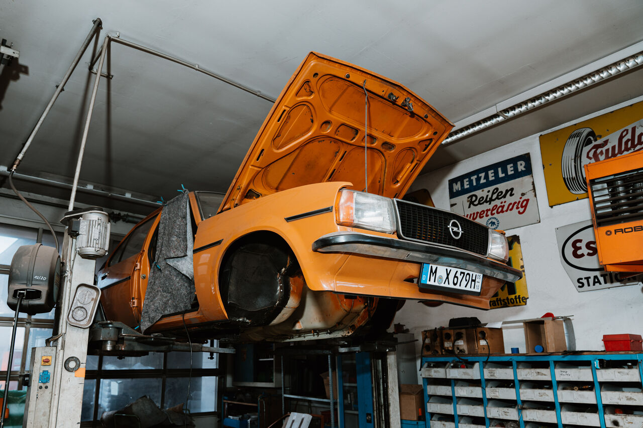 Oranger Oldtimer mit geöffneter Motorhaube auf der Hebebühne der Werkstatt